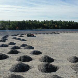 Many large piles of gravel are evenly distributed through an open area with a dump truck in the center.