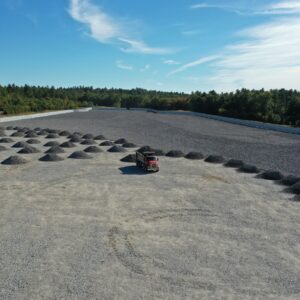 An aerial view of the Copart worksite with many large piles of gravel covering half of the fenced in area. There is a dump truck in the center dropping off more gravel.