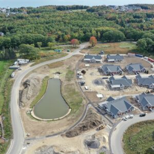A high up aerial view of the piper Shores worksite showing eight buildings under construction as well as winding roads and multiple ponds. The worksite has large piles of dirt and gravel as well as construction materials. The ocean is visible in the distance.