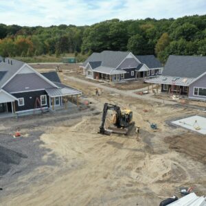 An aerial view of a section of the Piper Shores worksite showing four buildings under construction with an excavator in the middle of an open area surrounded by piles of gravel and dirt.