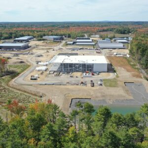 A high up aerial view of the IDEXX worksite. There is a large building under construction in the center of an open area which has construction equipment throughout.