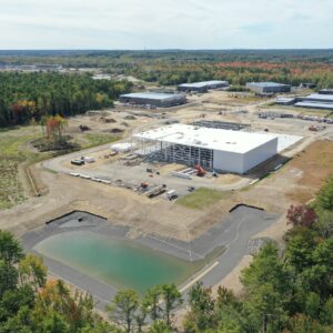 A high up aerial view of the IDEXX worksite with a reservoir in the foreground, a large building under construction in the middle, and several other large buildings in the background.