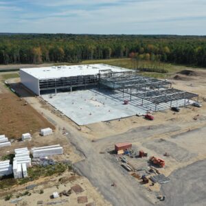 An aerial view of the IDEXX worksite. A large building in the center is under construction and there is heavy metal framing being built. Many construction cones are places around the worksite.