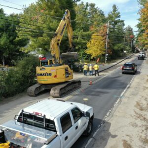 A road with the pavement removed from one lane with an excavator parked in the foreground